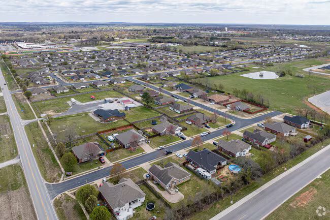 Aerial view of a suburban neighborhood with houses, roads, lawns, and open fields