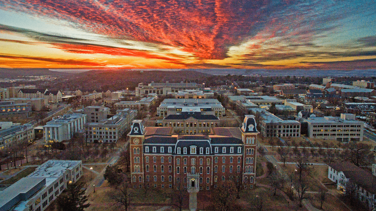 Aerial view of a campus at sunset, with red-orange clouds over historic buildings and tree-lined streets.