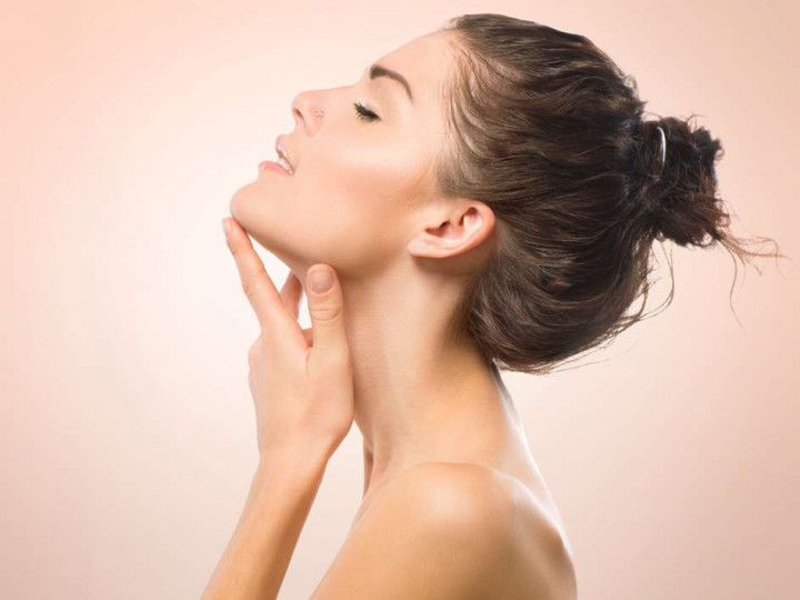 Woman touching her neck in profile against a soft pink background
