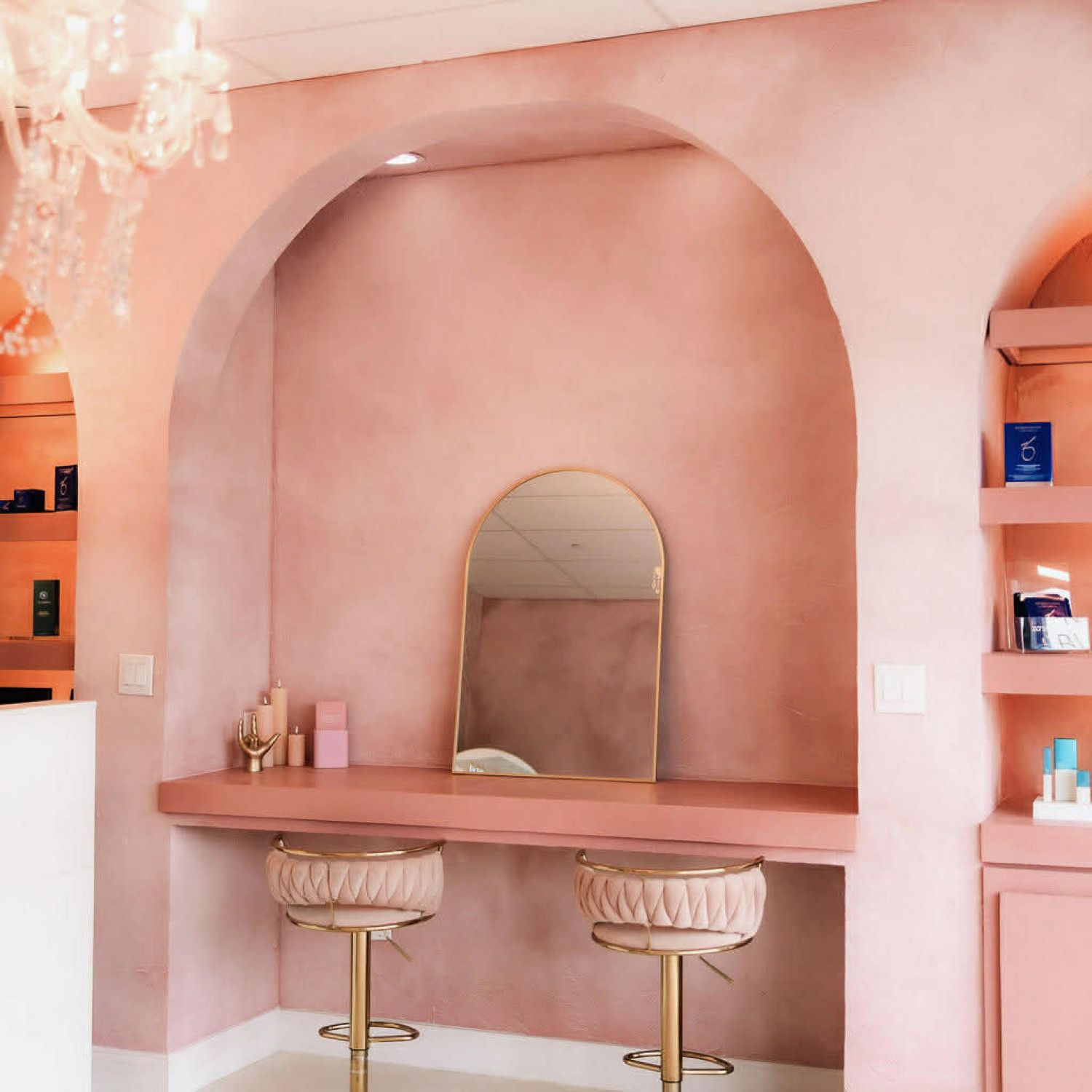 Pink vanity nook with arched wall, mirror, and two gold stools in a soft blush room