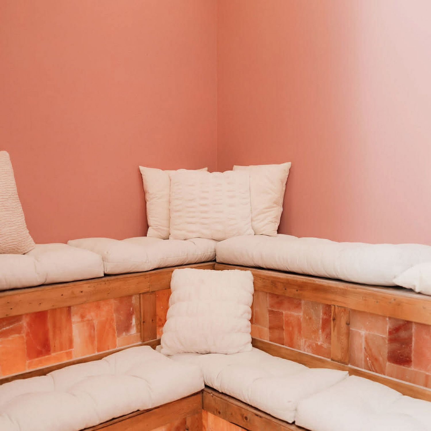 Cozy corner bench with white cushions and brick base against soft pink walls