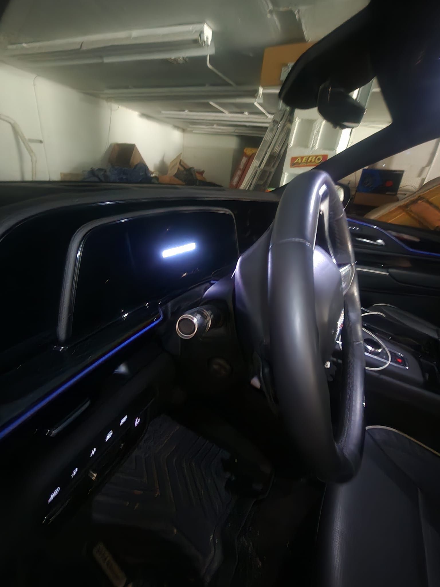Black car interior with steering wheel, illuminated dashboard, and blue accent lighting.