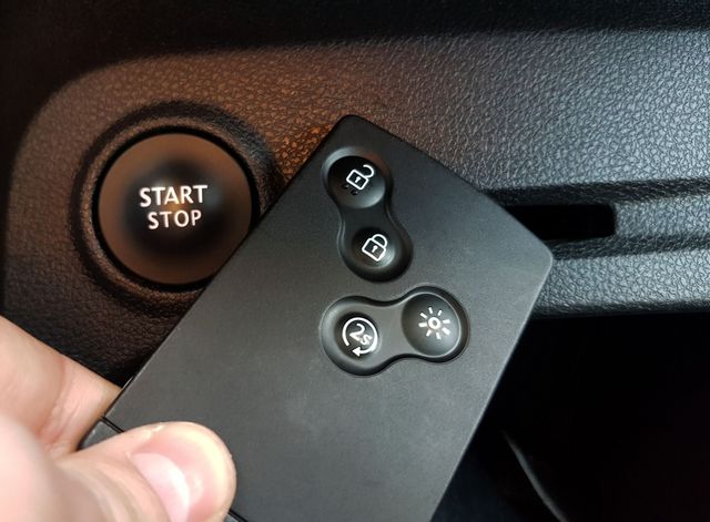 Hand holding car key fob near start/stop button. Black key fob with unlock, lock, and other buttons.