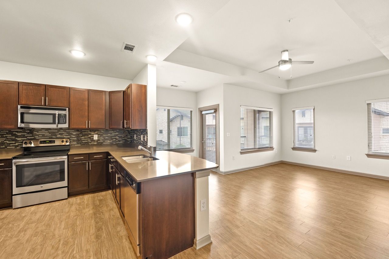 Open-concept kitchen with dark wood cabinets, stainless steel appliances, and a bright living area with multiple windows.