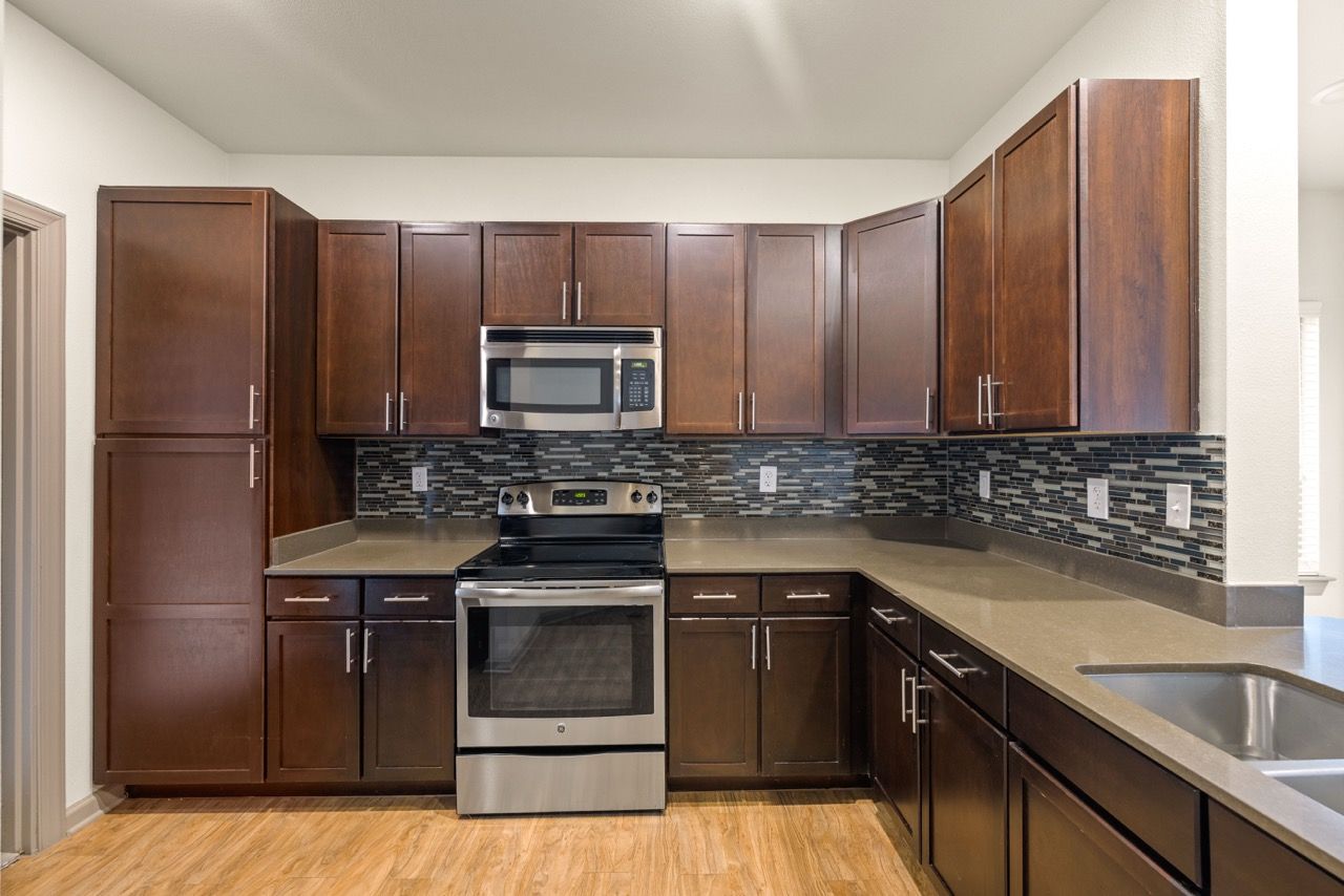 Modern apartment kitchen with dark wood cabinets, stainless-steel appliances, and a glass tile backsplash.