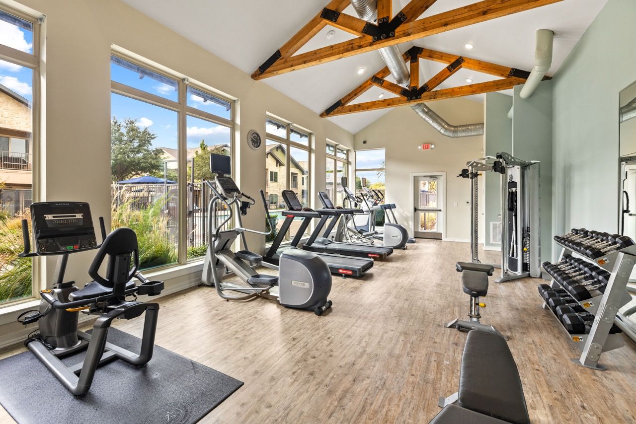 Bright community gym with cardio machines and free weights by large windows.