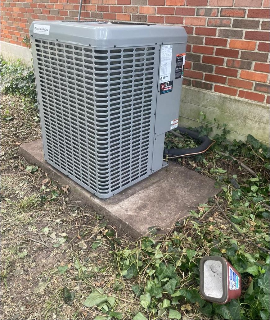 Outdoor air conditioning unit beside a brick house, with a small light on the ground nearby.