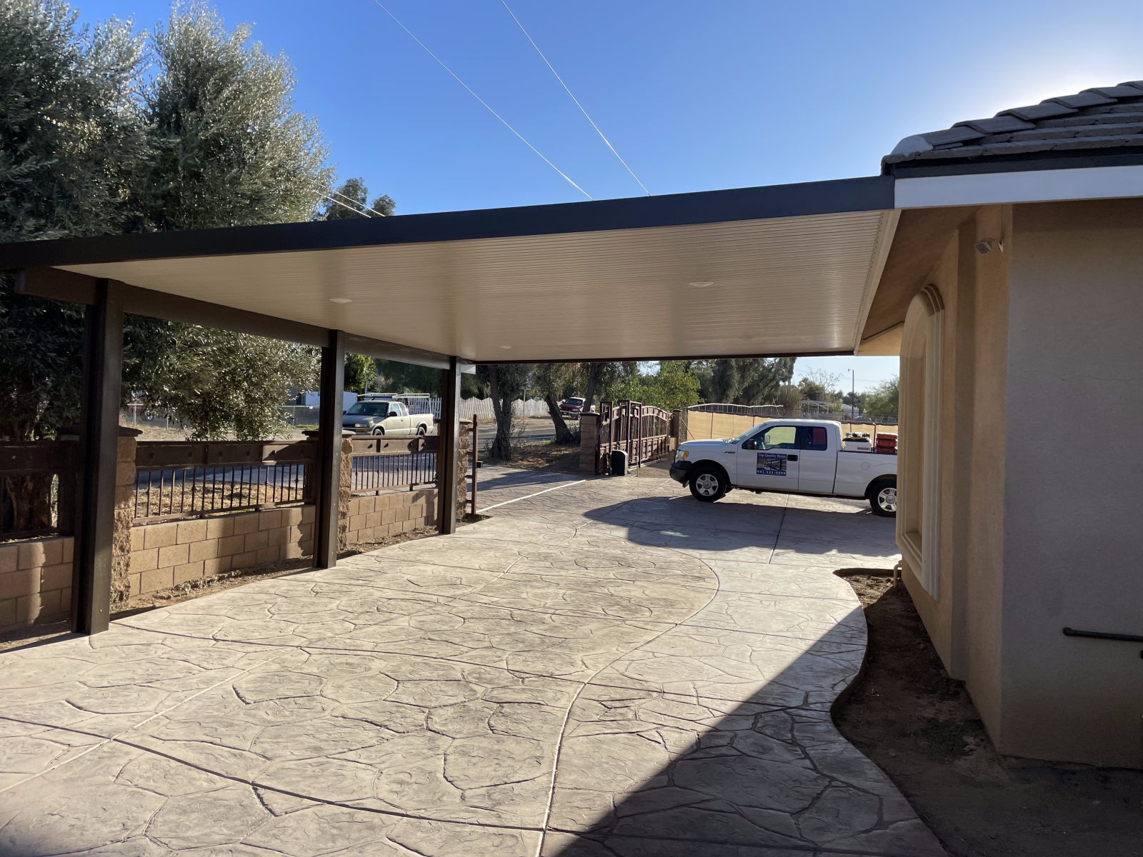 Carport with stamped concrete driveway; white truck parked; beige building.