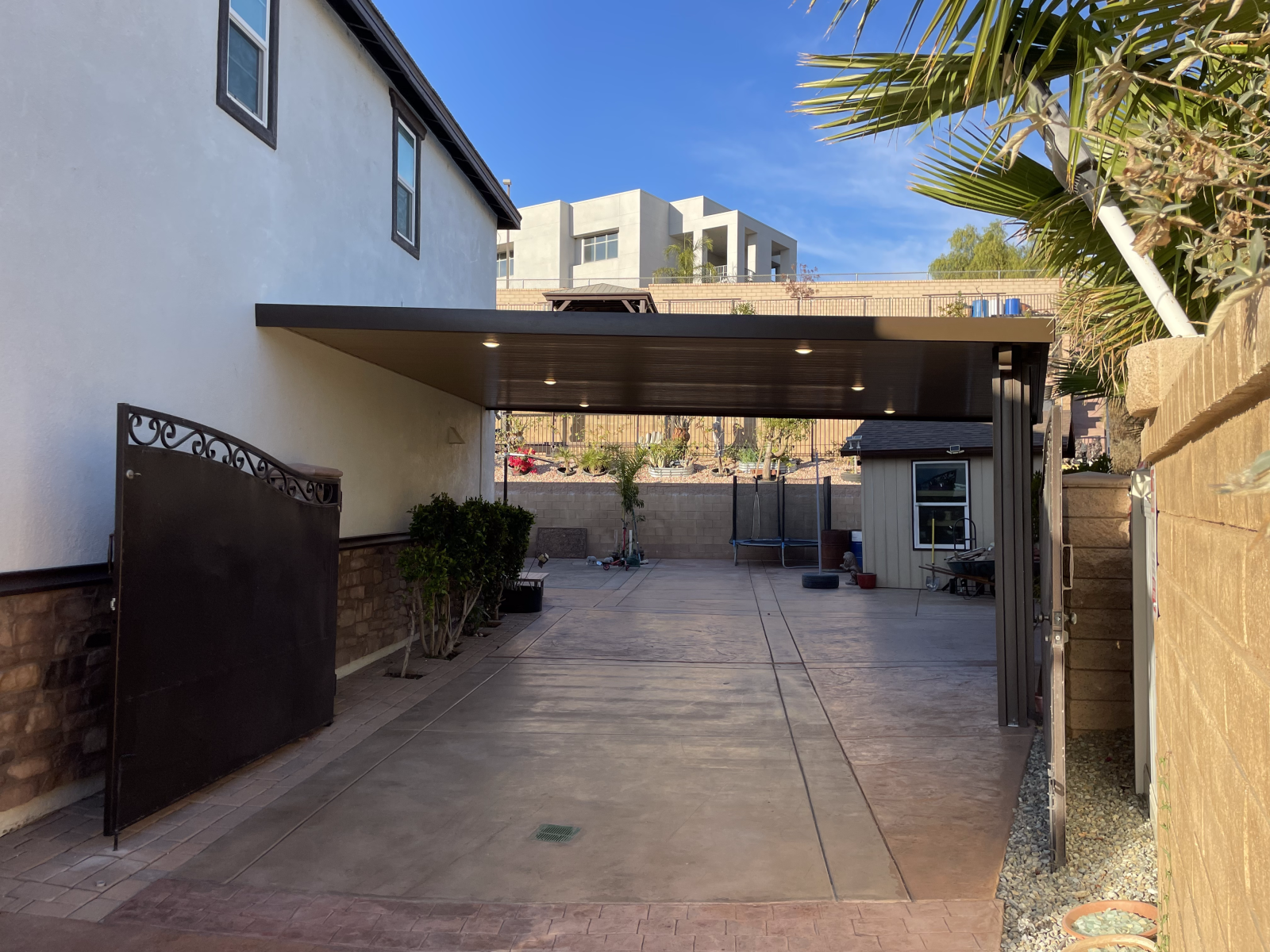 Brown carport attached to a light-colored building, leading to a concrete driveway.