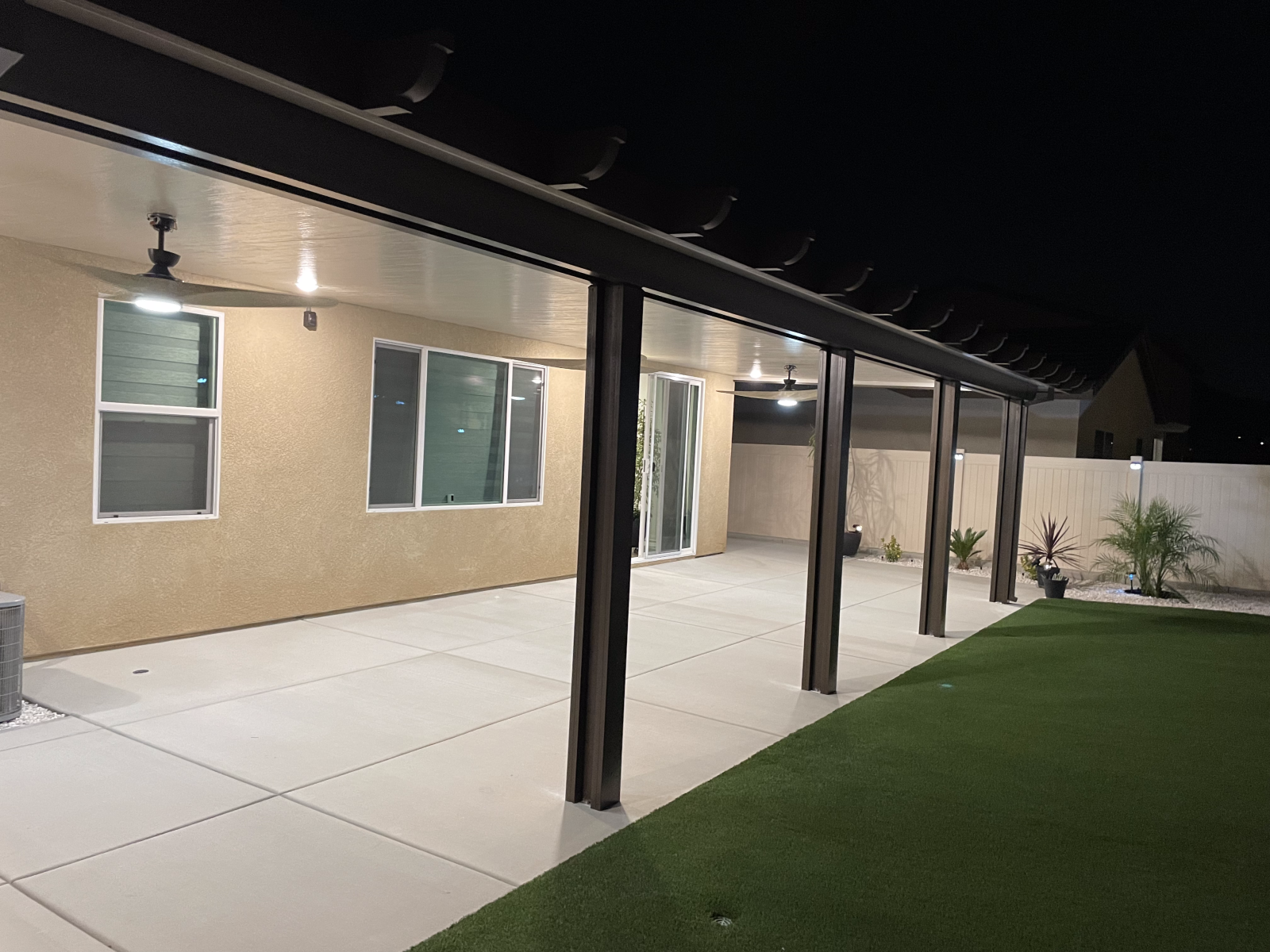 Patio with a dark awning, columns, and a grassy yard at night.