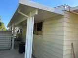 Beige siding with a white roof overhang supported by white columns. A black trash can sits below.