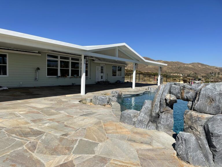 House with patio, pool, and rock formation, under a clear blue sky.