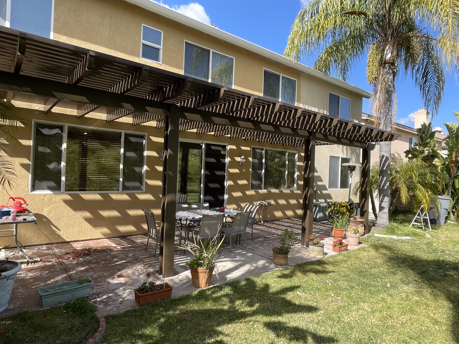 Backyard with a pergola over a patio, lawn, and two-story house.