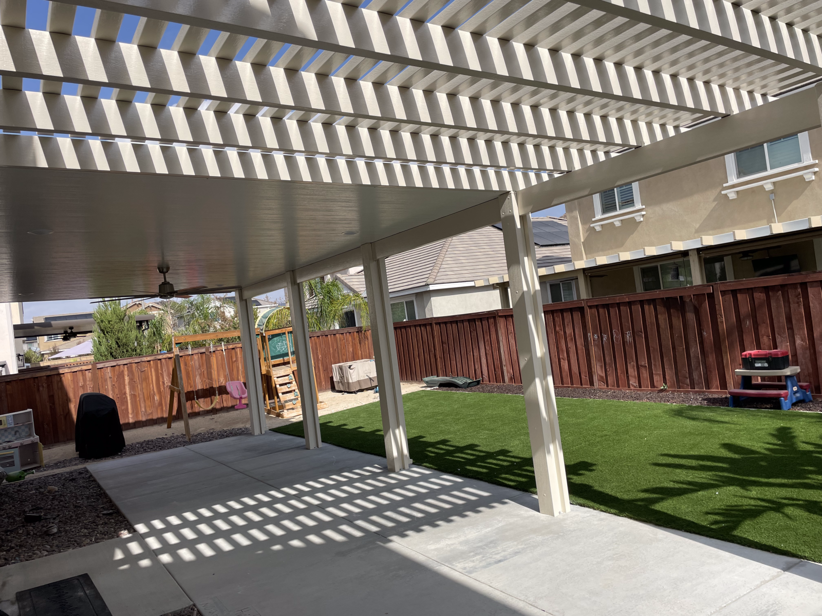 Covered patio with white beams and concrete floor overlooking a grassy yard.