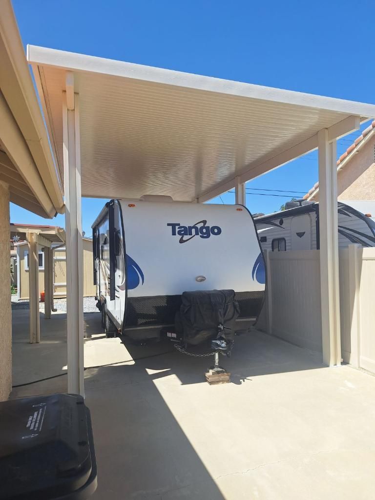 RV trailer parked under a white carport with a corrugated ceiling.