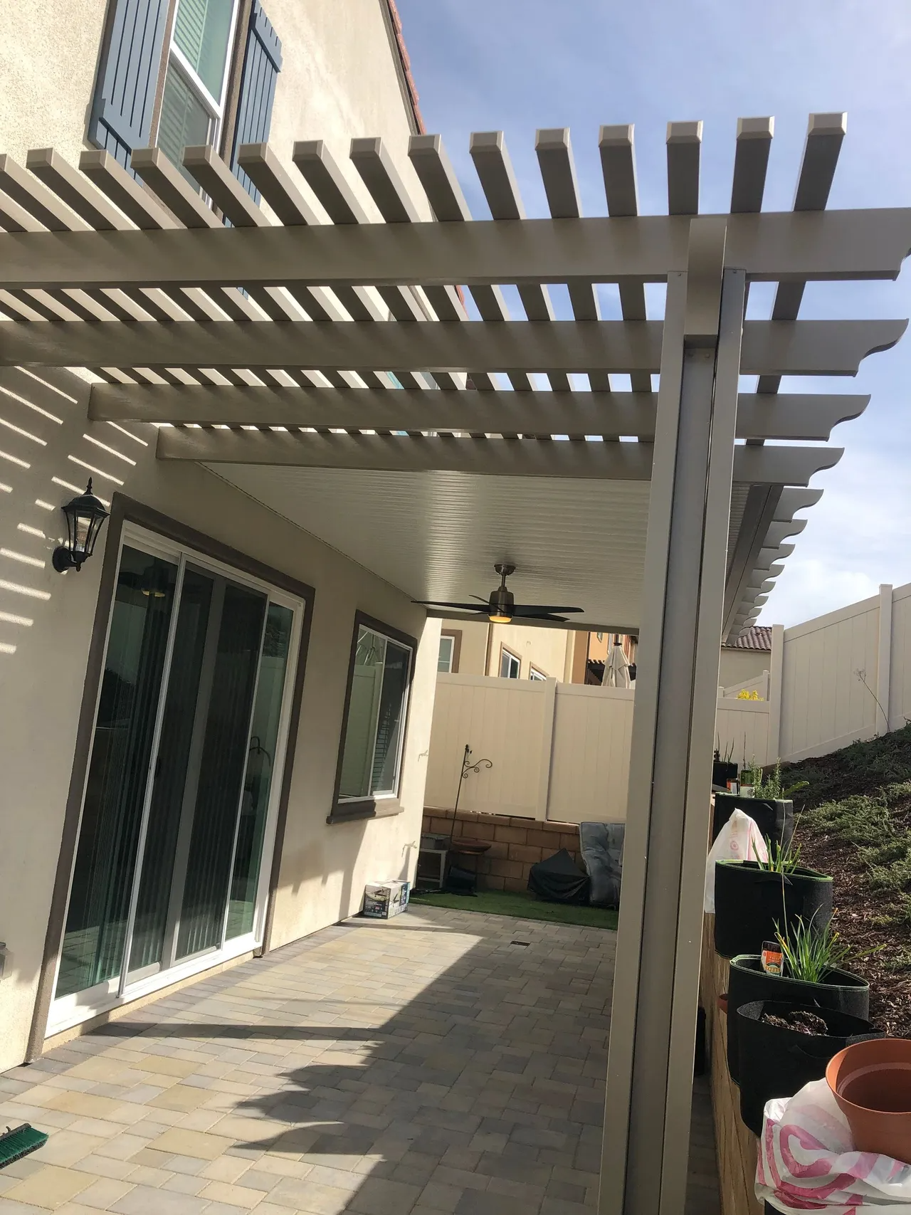 Pergola over a patio with sliding glass doors, a ceiling fan, and a light-colored exterior wall.