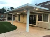 Patio with a white aluminum cover, supported by columns, adjacent to a house with sliding glass doors.