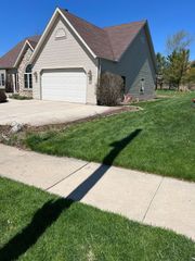 Suburban house with beige siding, brown roof, garage, and green lawn on a sunny day