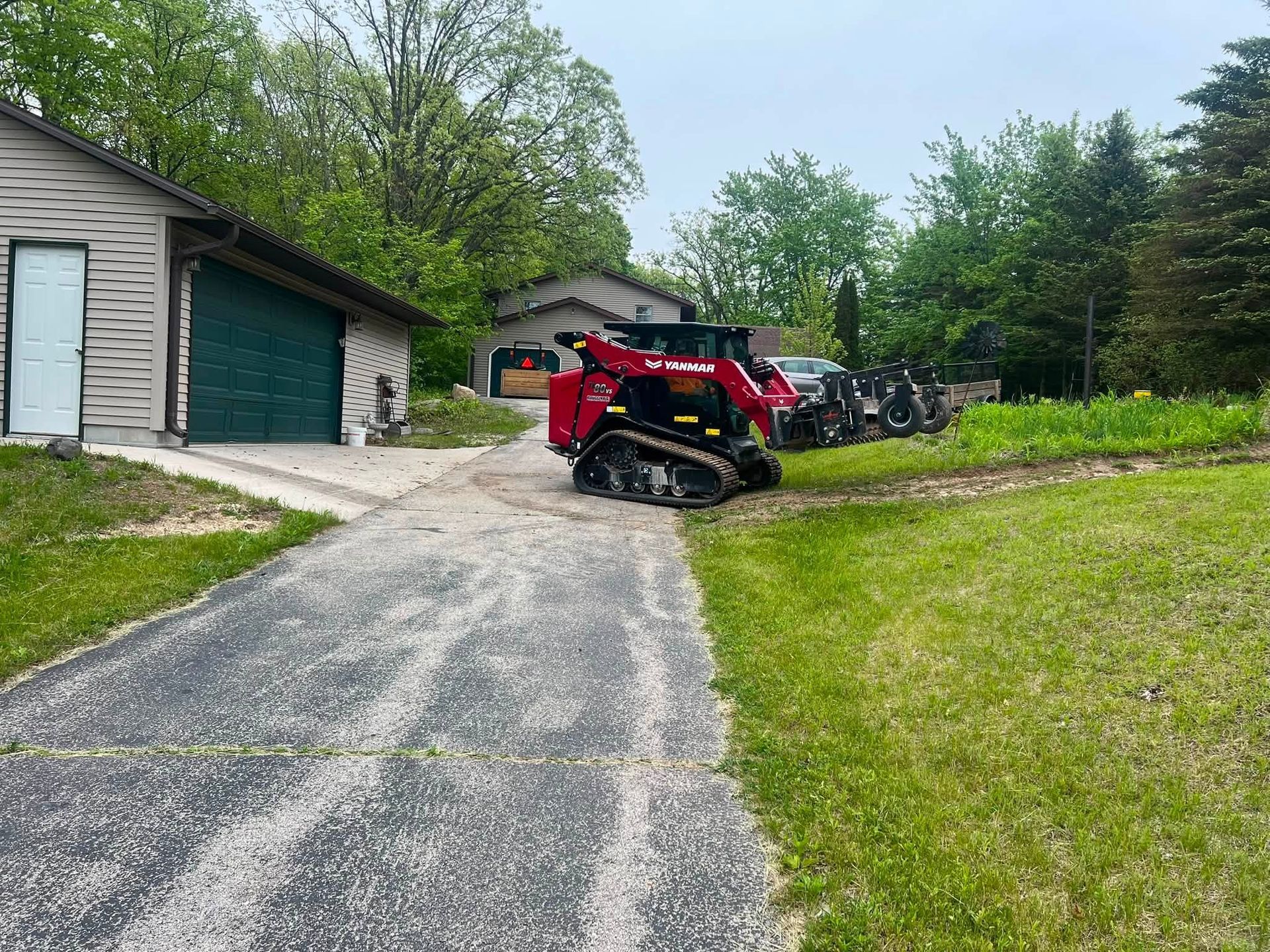 Red tractor with mower on a gravel driveway beside a garage in a suburban yard