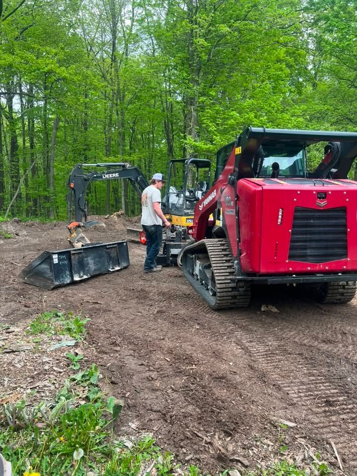 Workers beside a red forestry machine clearing a dirt path in a green wooded area