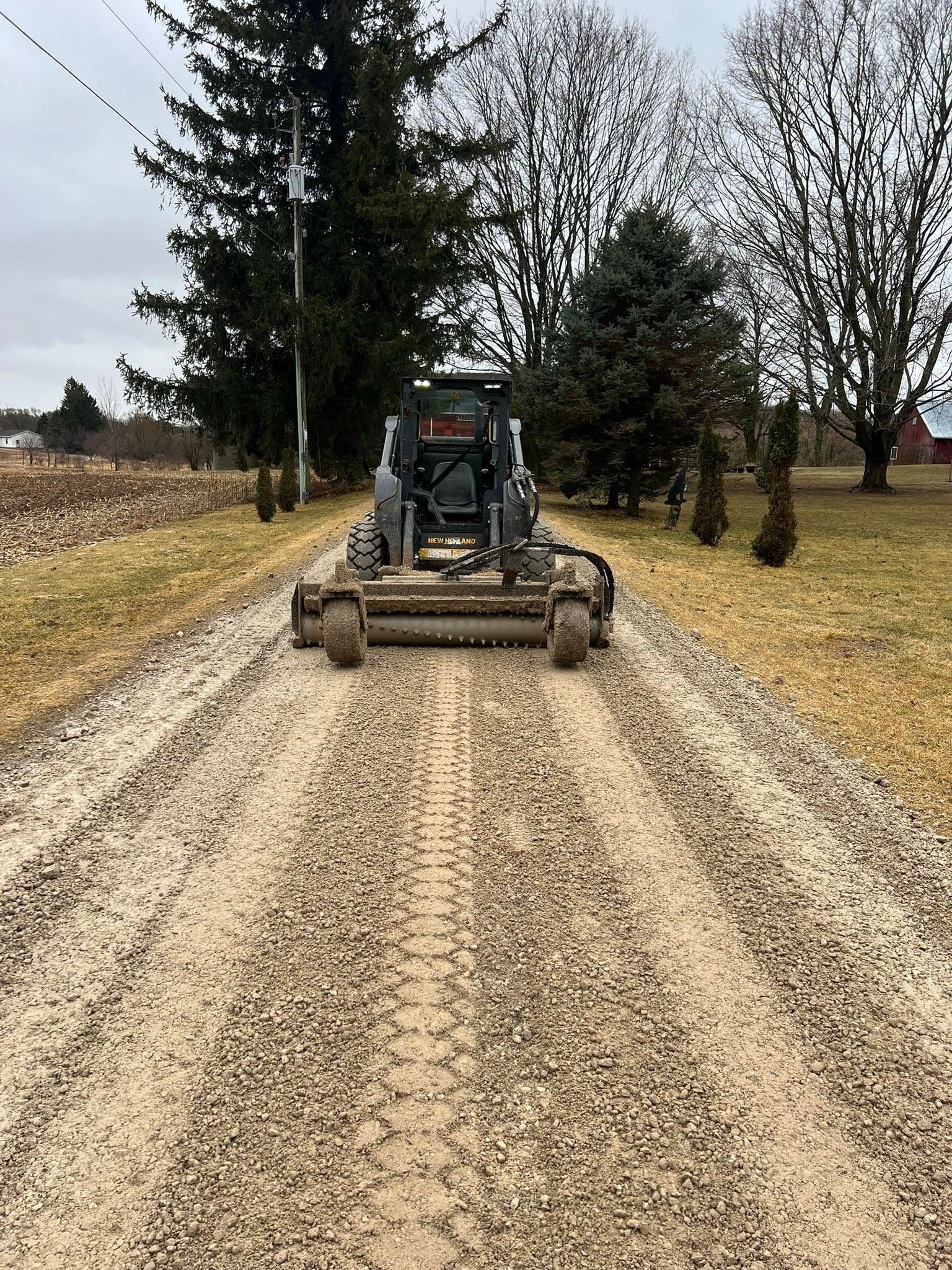 Tractor driving down a gravel farm lane between bare trees and fields