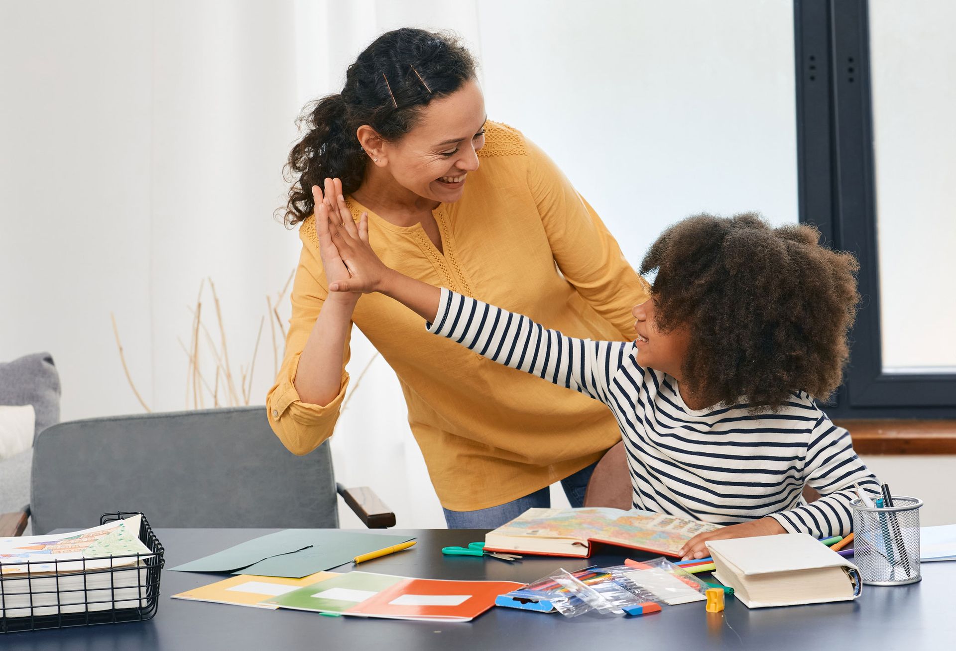 A woman is giving a child a high five while sitting at a table.