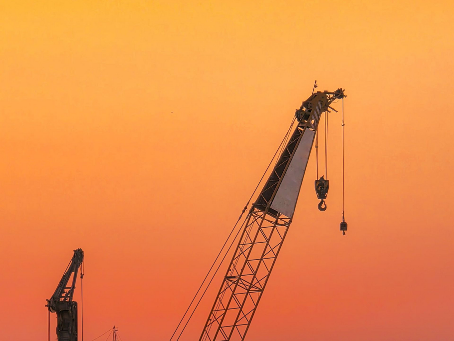 The top of a few cranes with the sunset in the background.