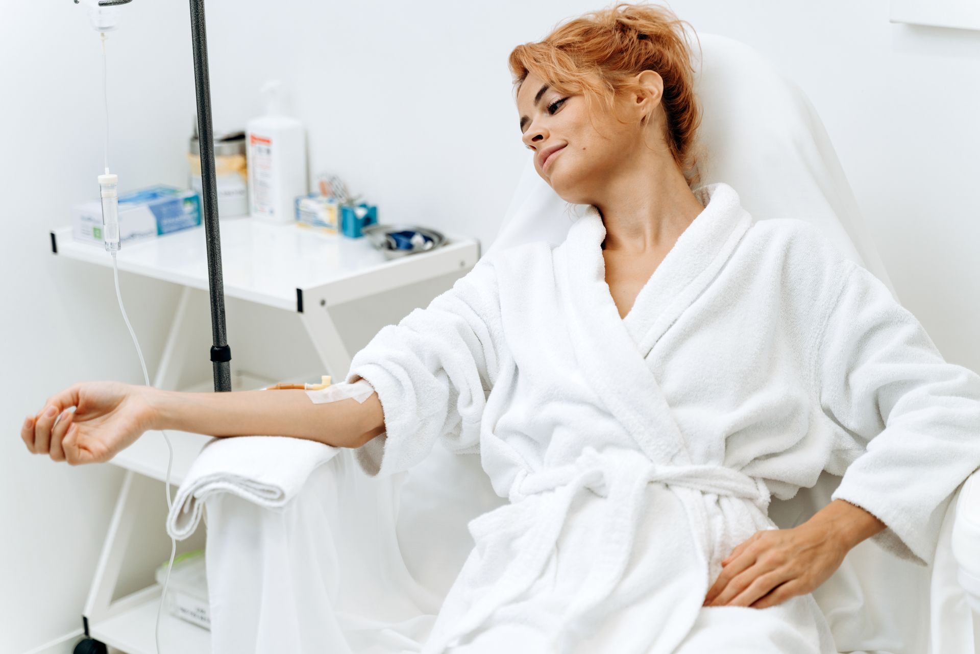 IV Therapy Smiling woman in a white robe reclining in a chair during an IV therapy treatment infusion session.