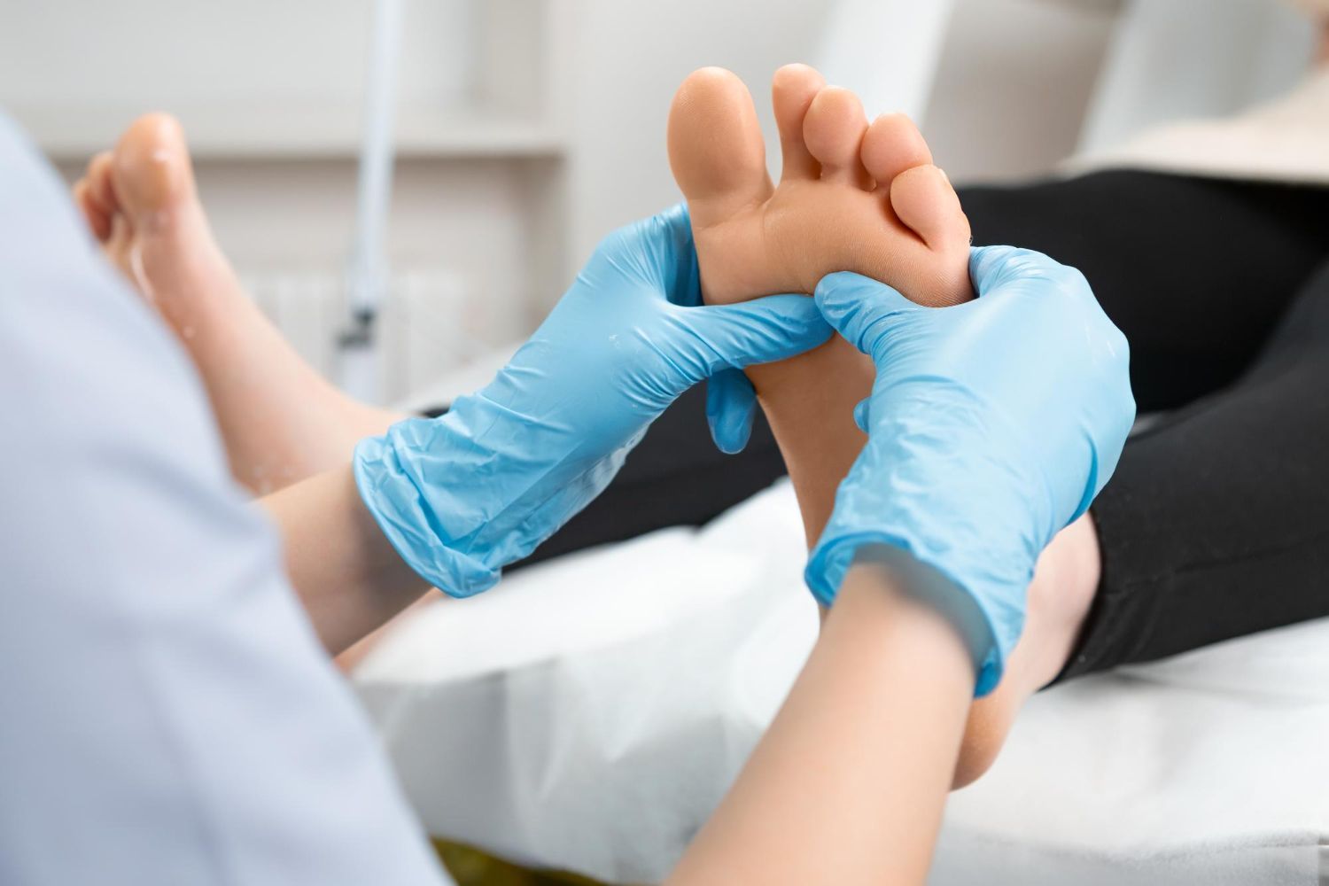 Blue-gloved hands gently examining a patient’s foot in a clinical setting