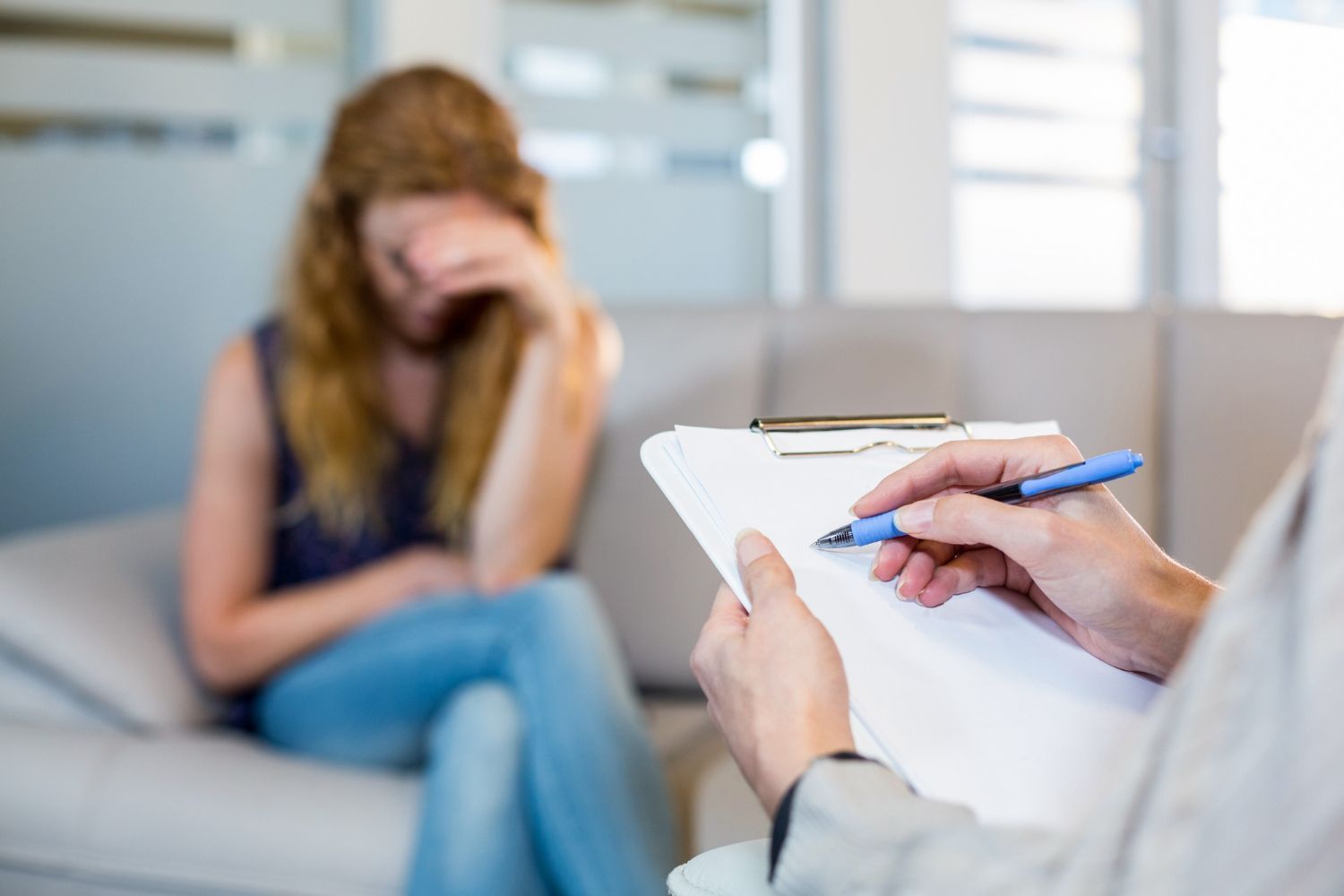 Therapist taking notes while a distressed client sits on a couch in a 상담 room