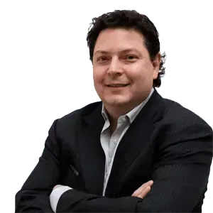 A man in a suit is sitting with his arms crossed and smiling.