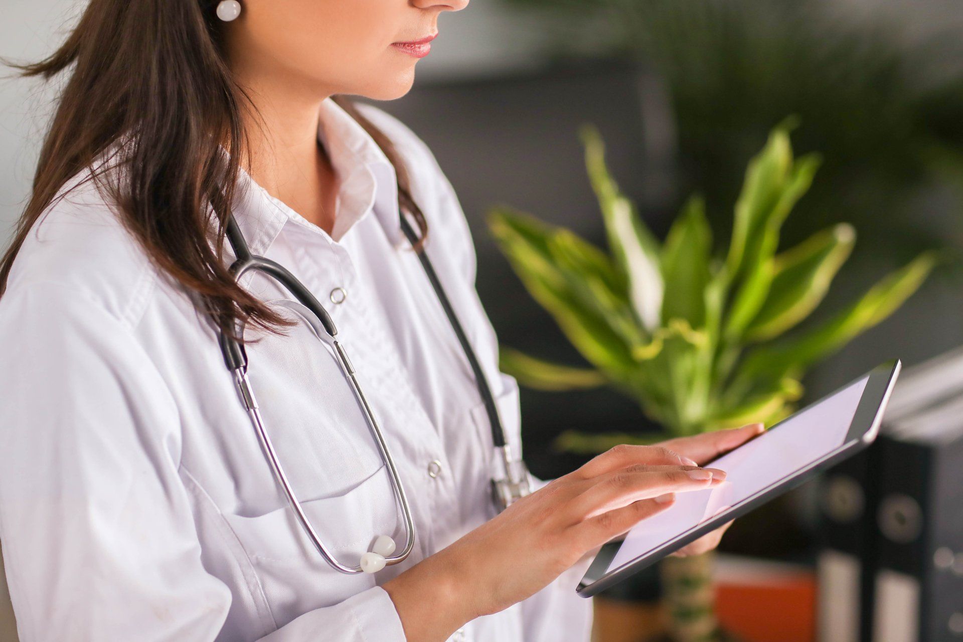 Woman in a white blouse using a tablet in an office setting with a green plant in the background