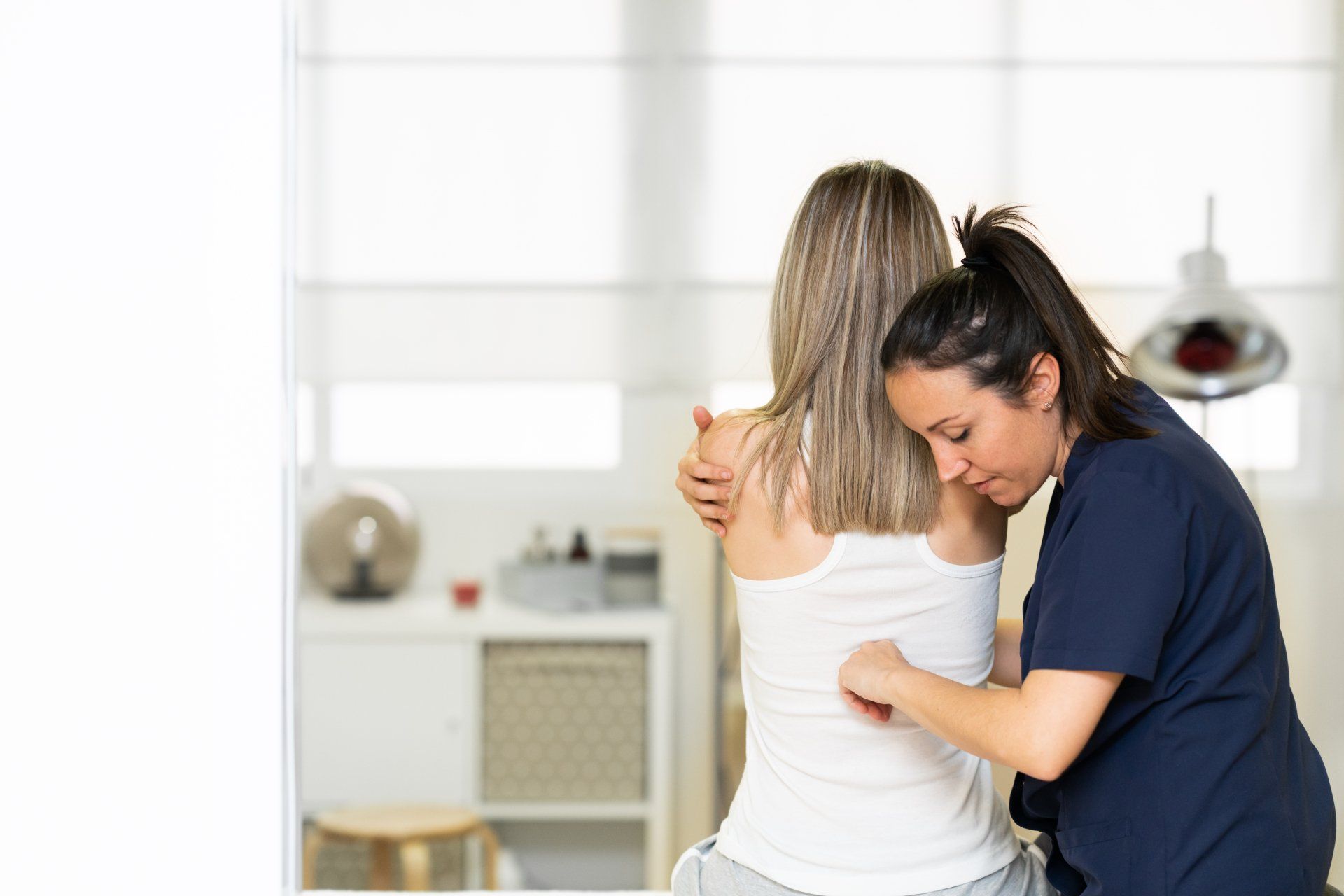 Two women embracing in a bright kitchen, one comforting the other with a hand on her back