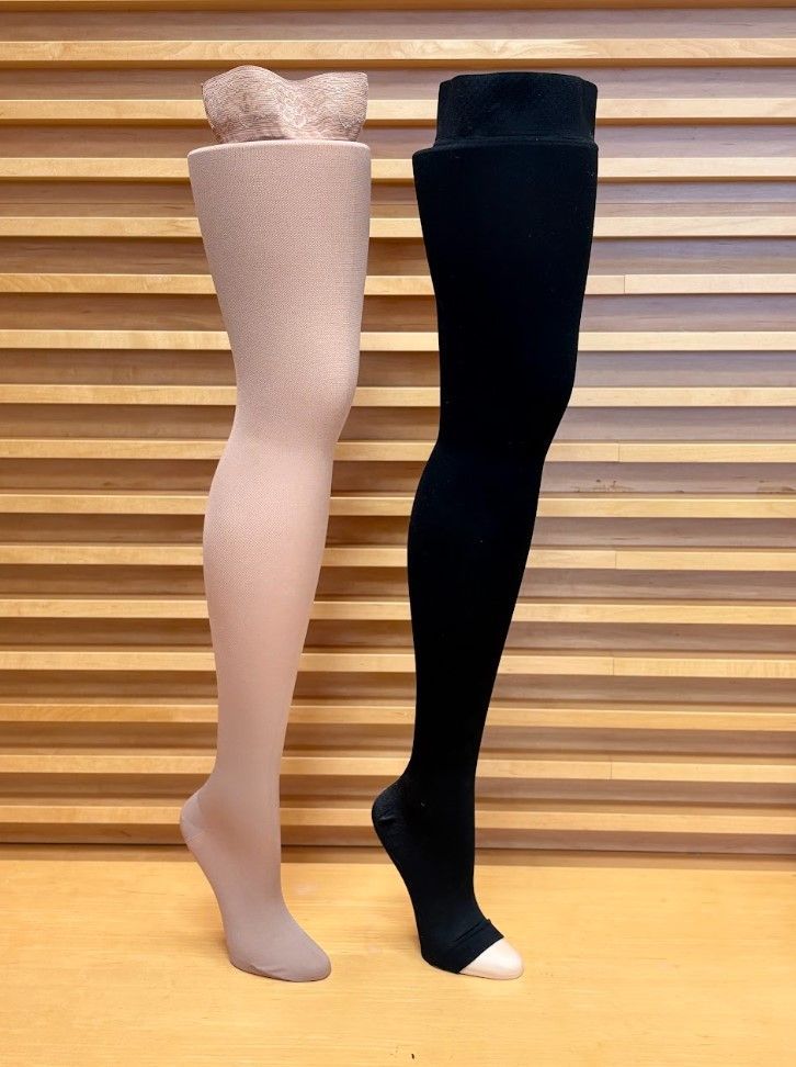 Two mannequin legs wearing light pink and black hosiery, displayed side by side on a wooden floor.