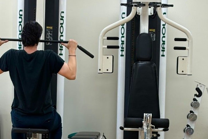 Person using a lat pulldown machine in a gym, viewed from behind, with black and white equipment.