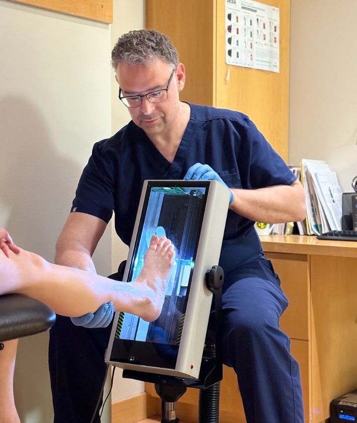 Podiatrist examining a patient's foot with a medical imaging screen in a clinic room