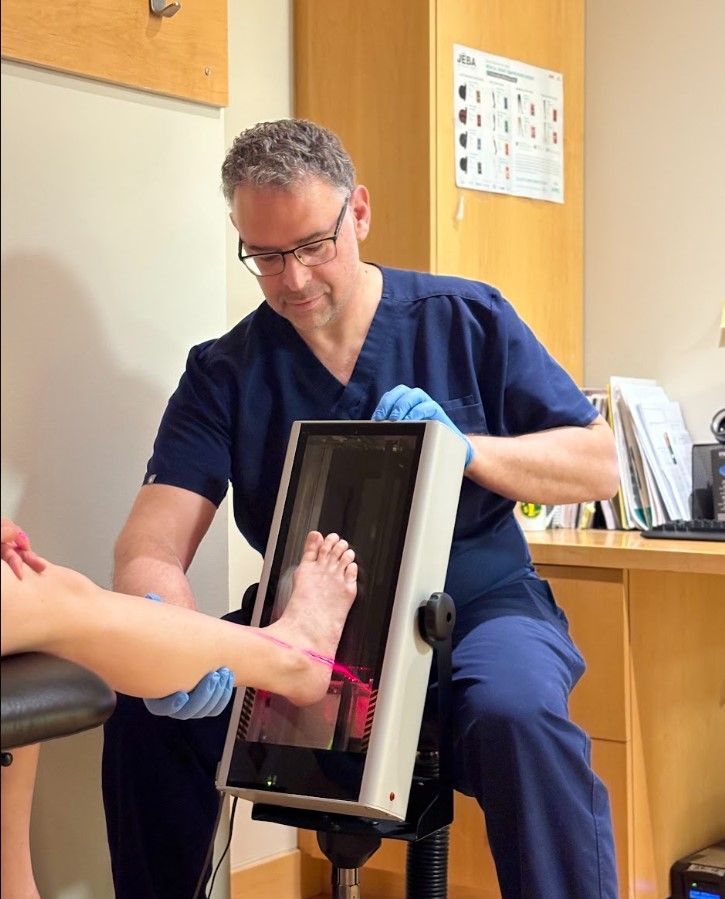 Clinician using a handheld device to examine a patient’s foot in a medical office