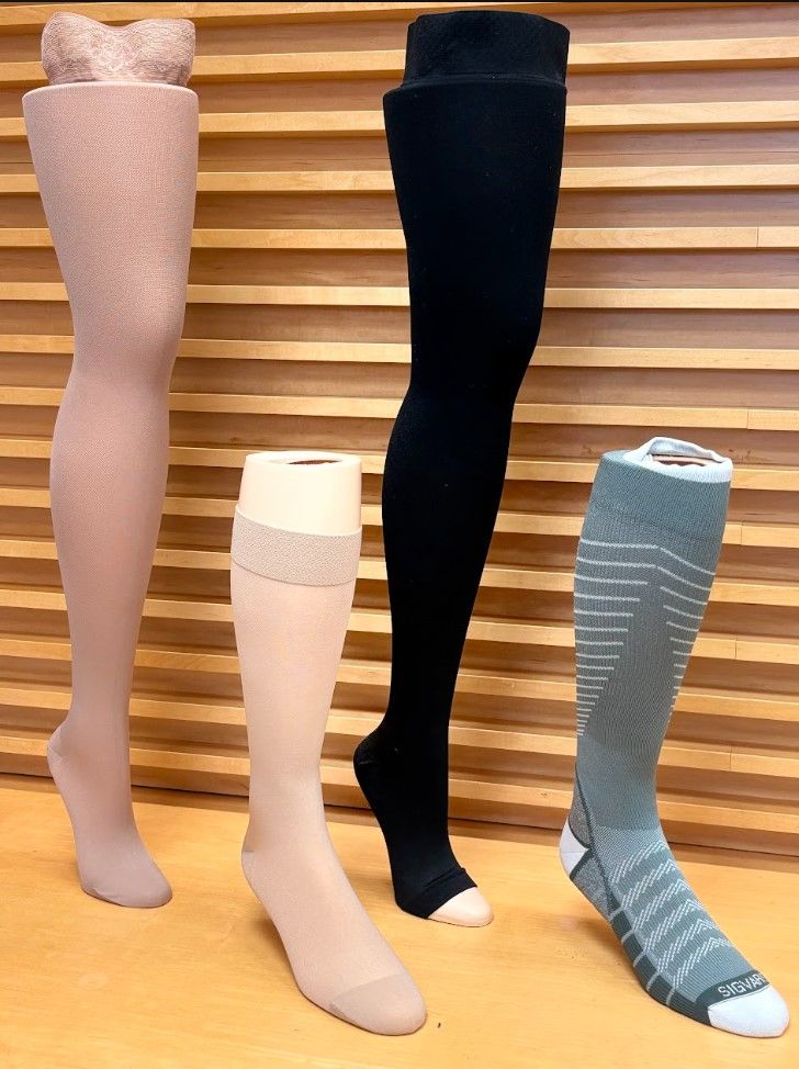 Four mannequin legs in different colored stockings on a wooden slat background.