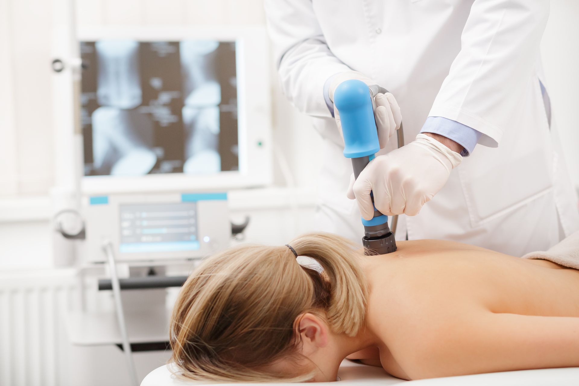 Healthcare worker using a handheld treatment device on a patient lying face down in a clinic.