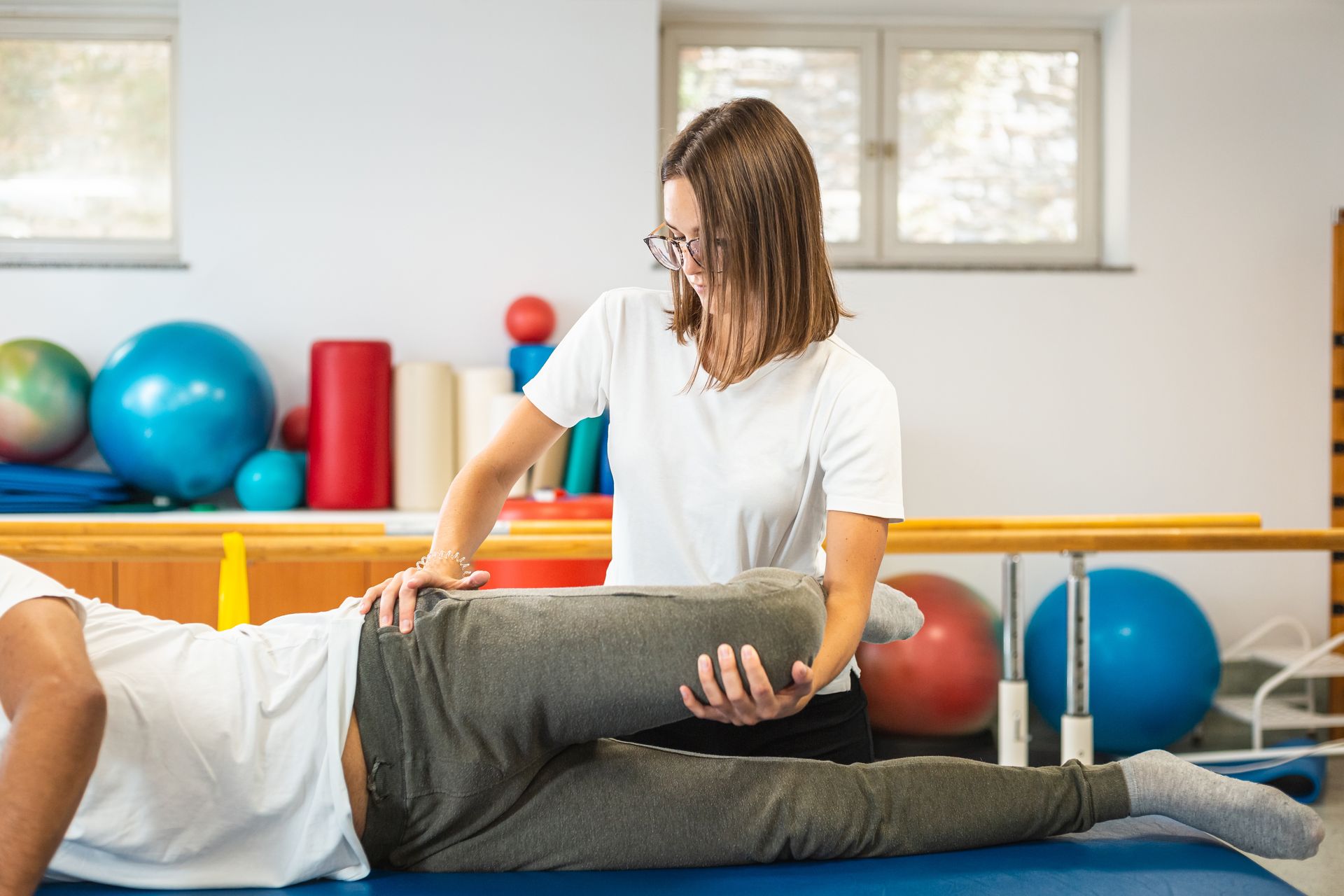Physical therapist assisting a patient stretching on a mat in a bright rehab room