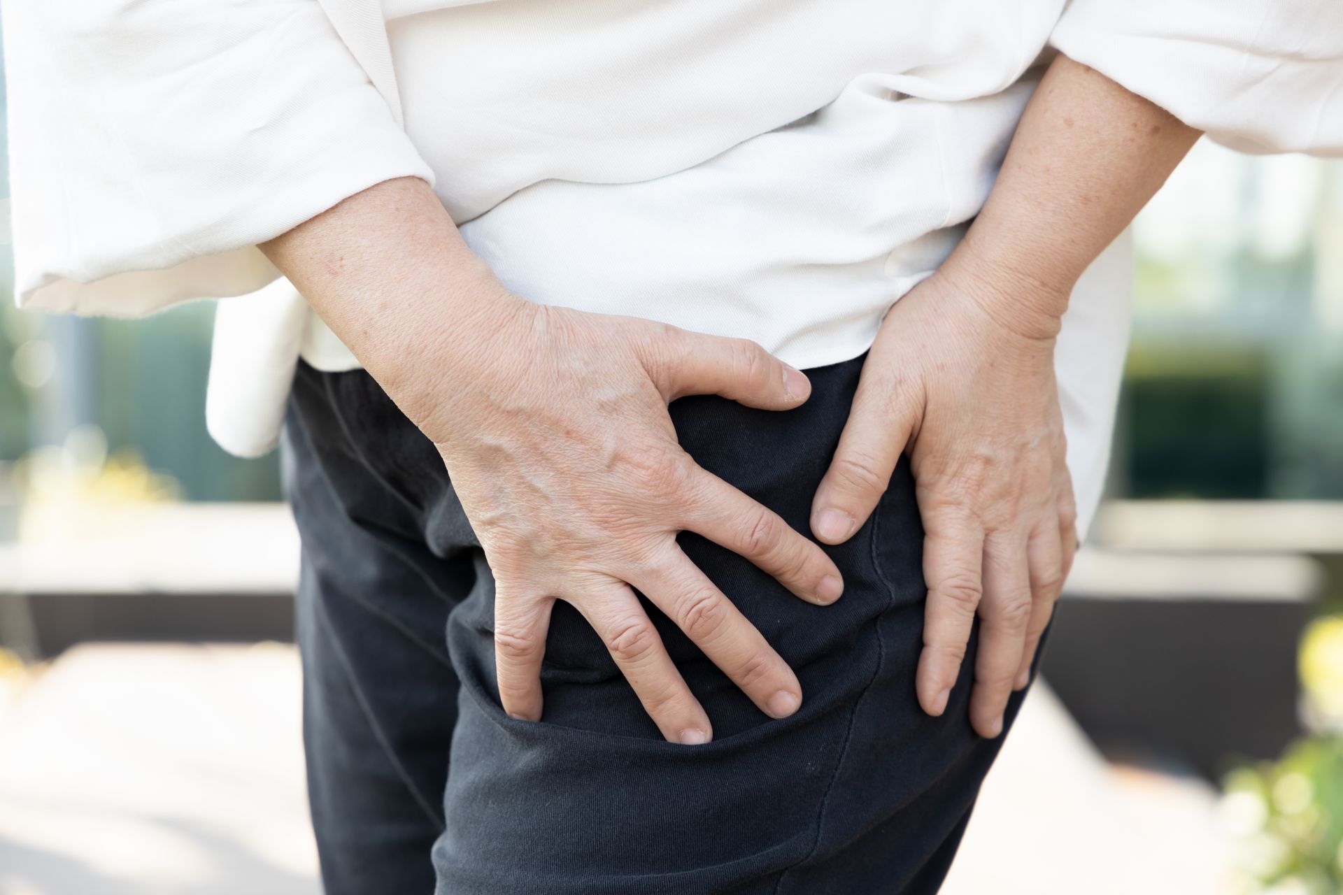 Close-up of a person holding their lower back with both hands, suggesting back pain.