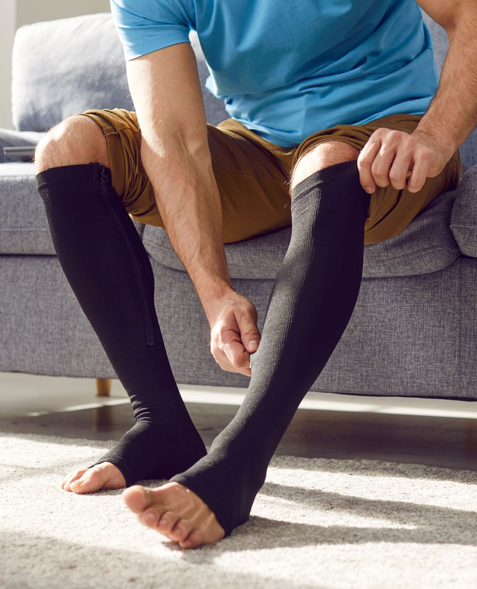 Person sitting on a couch pulling on a black knee-high sock