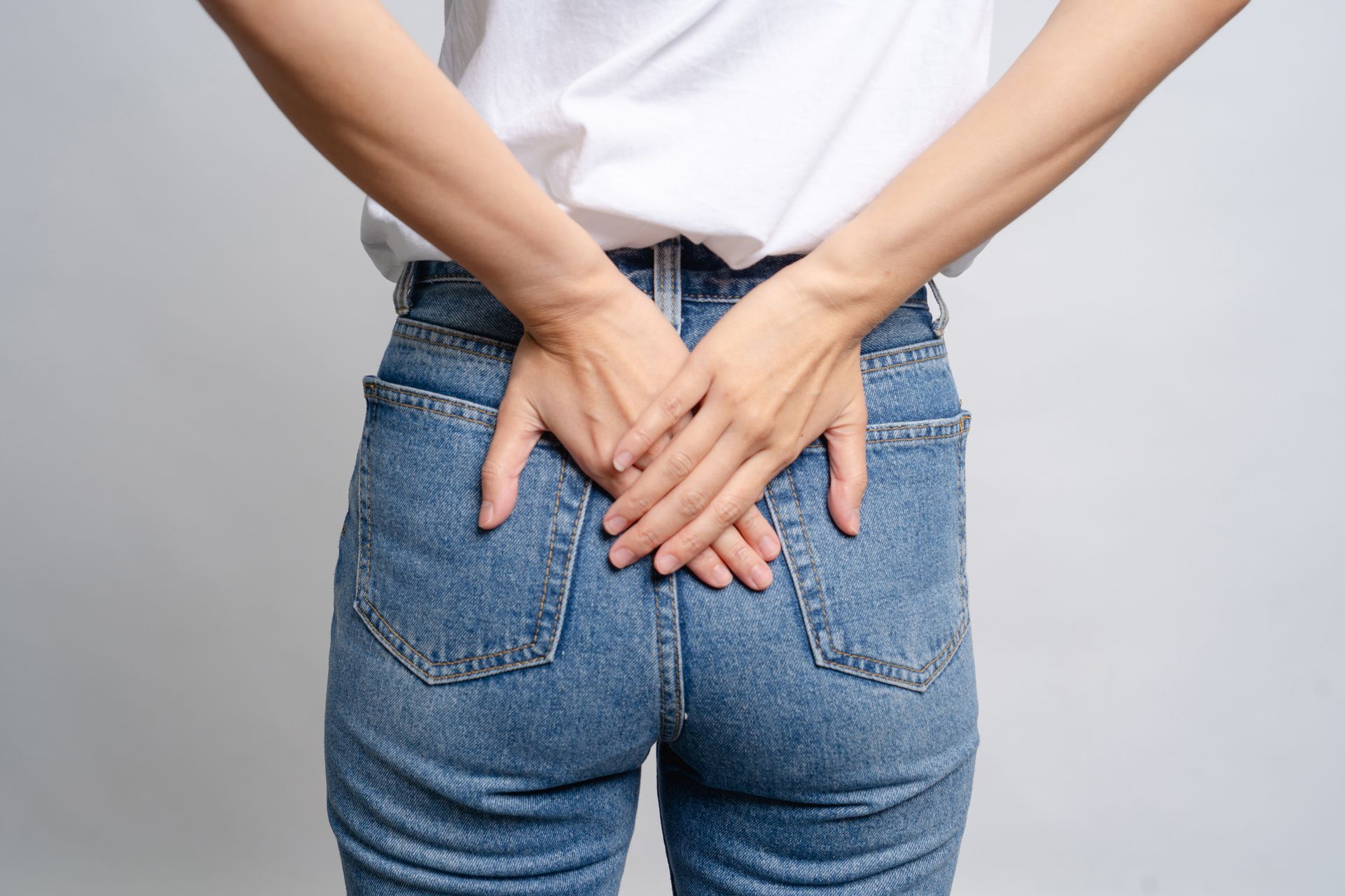 Person in blue jeans with hands clasped behind their back against a white background