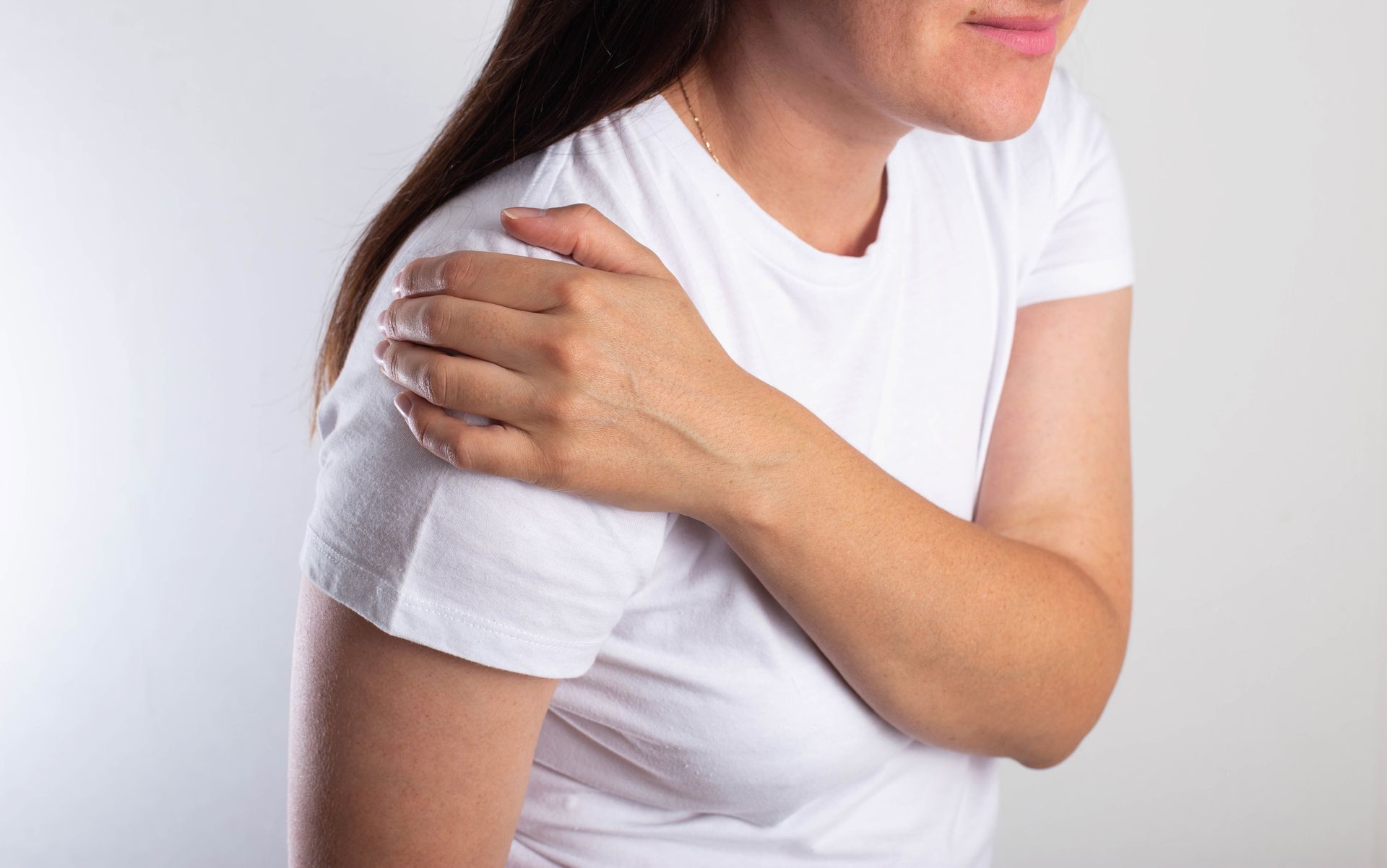 Woman in a white shirt holding her shoulder, suggesting pain or discomfort