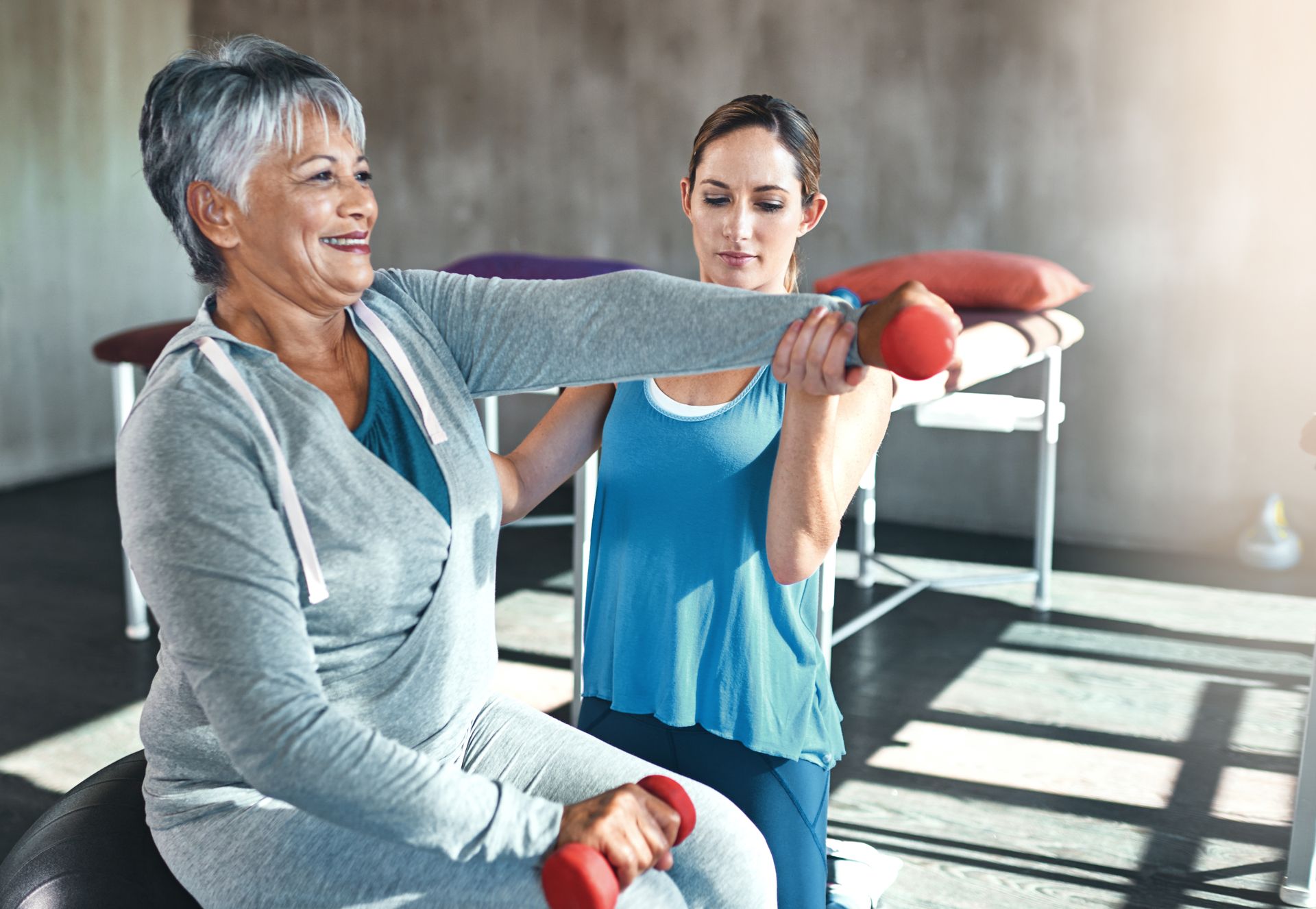 Two women doing a stretching exercise in a bright gym studio