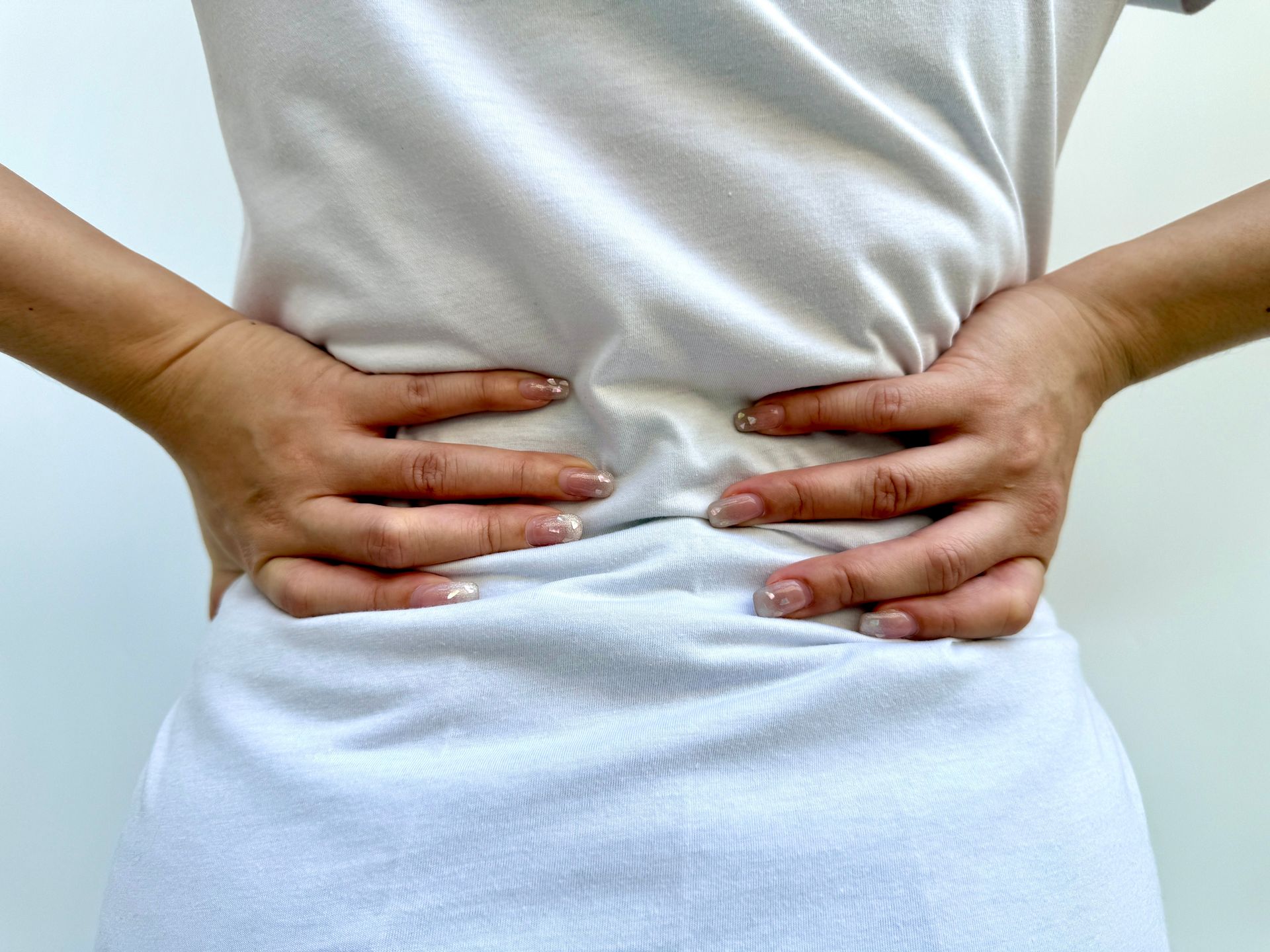 Hands pressing on the lower back of a person in a white shirt and light blue pants