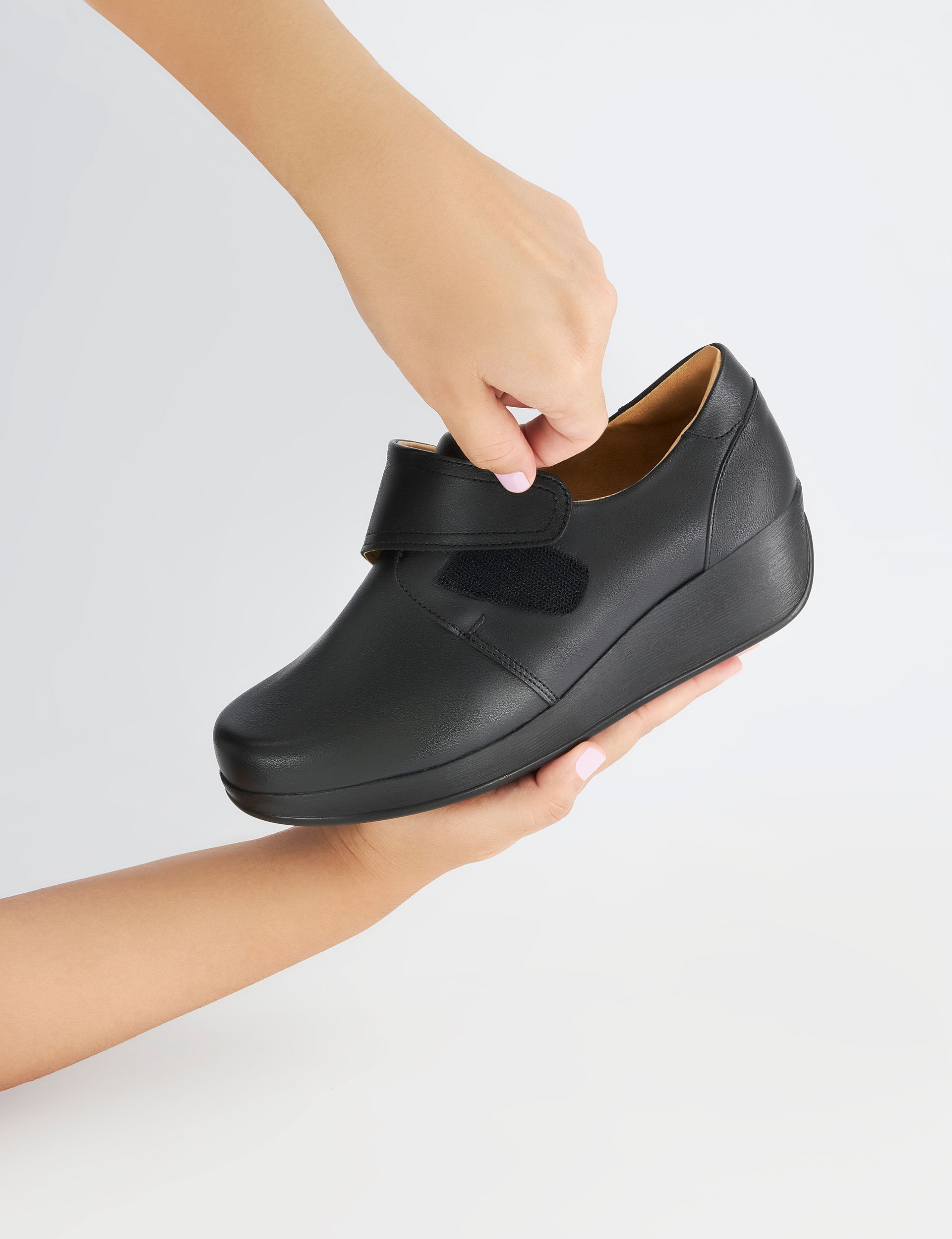 Hands holding a black children’s dress shoe with a strap, shown against a white background