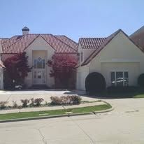 Suburban house with red tile roof, white stucco walls, and landscaped front yard on a sunny day