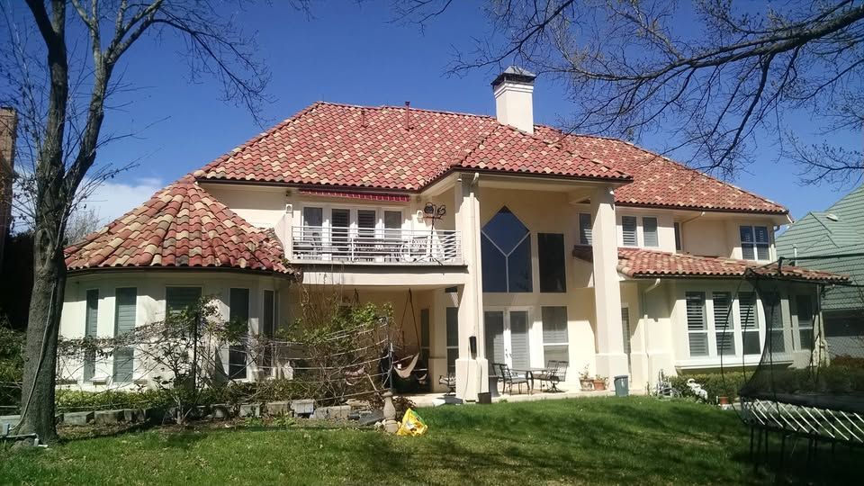 Large cream-colored house with a red tile roof, front lawn, and a central balcony on a sunny day
