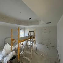 Renovation site with ladders, scaffolding, and covered furniture in a white room